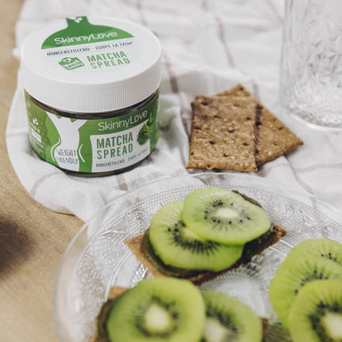 Potje matcha spread op een tafel met crackers en gesneden kiwi